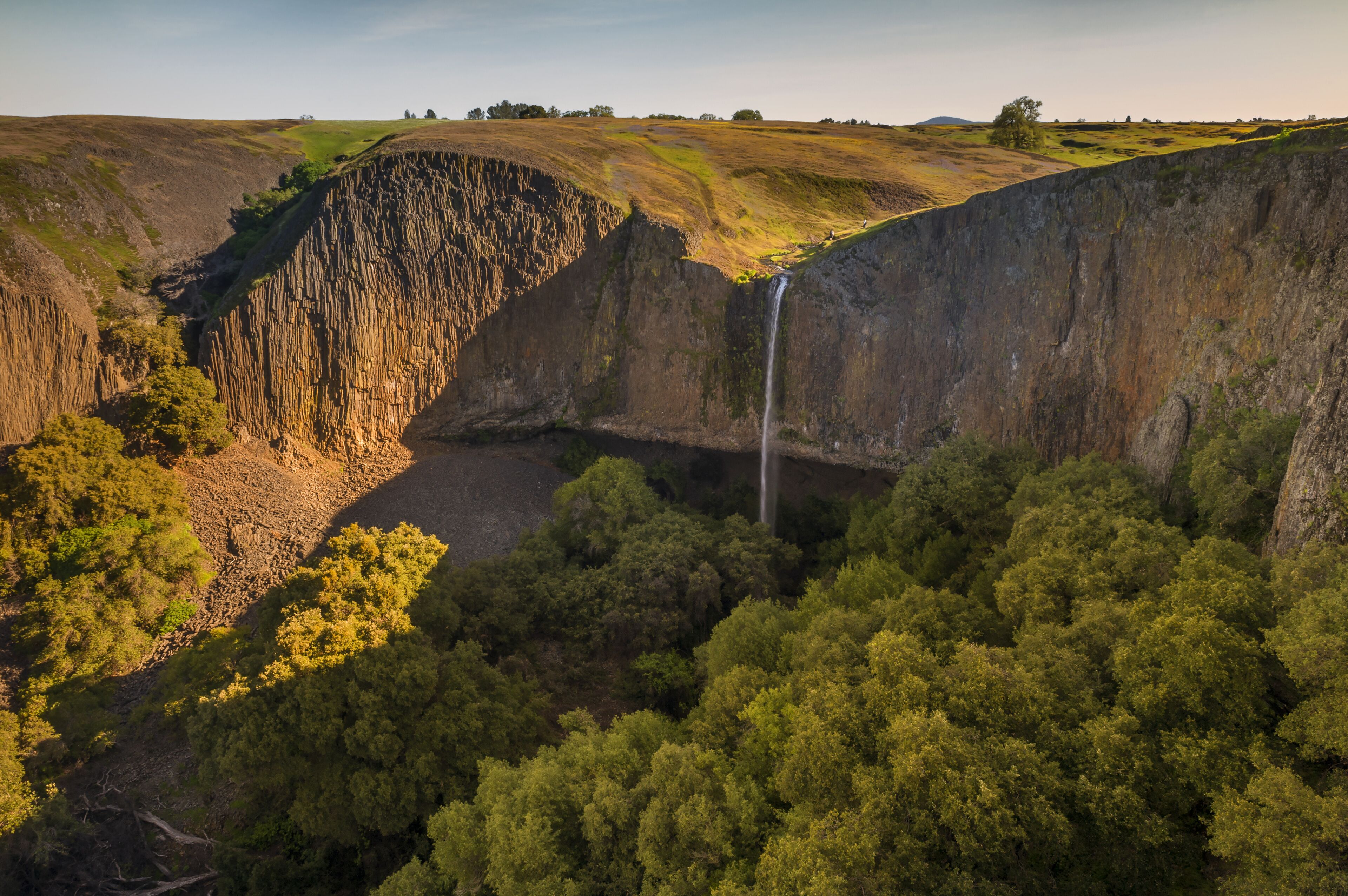 A waterfall cascading down a steep cliff surrounded by dense forest.
