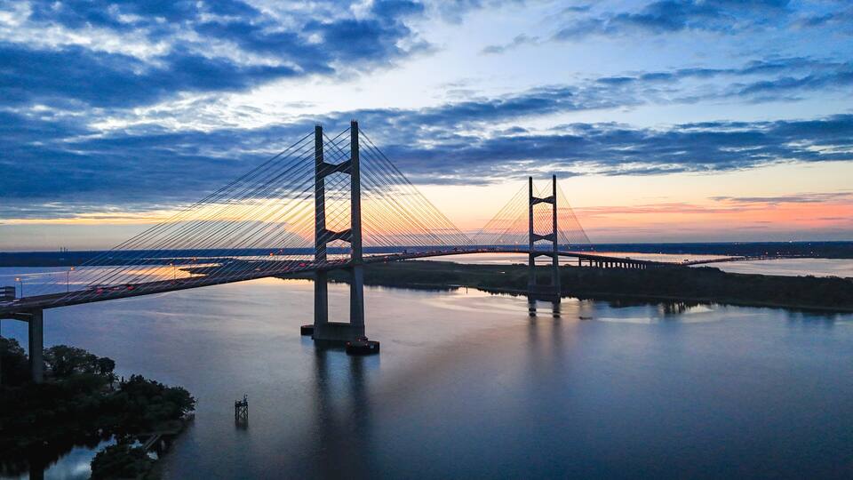 A suspension bridge over a calm body of water with a sunset in the background.