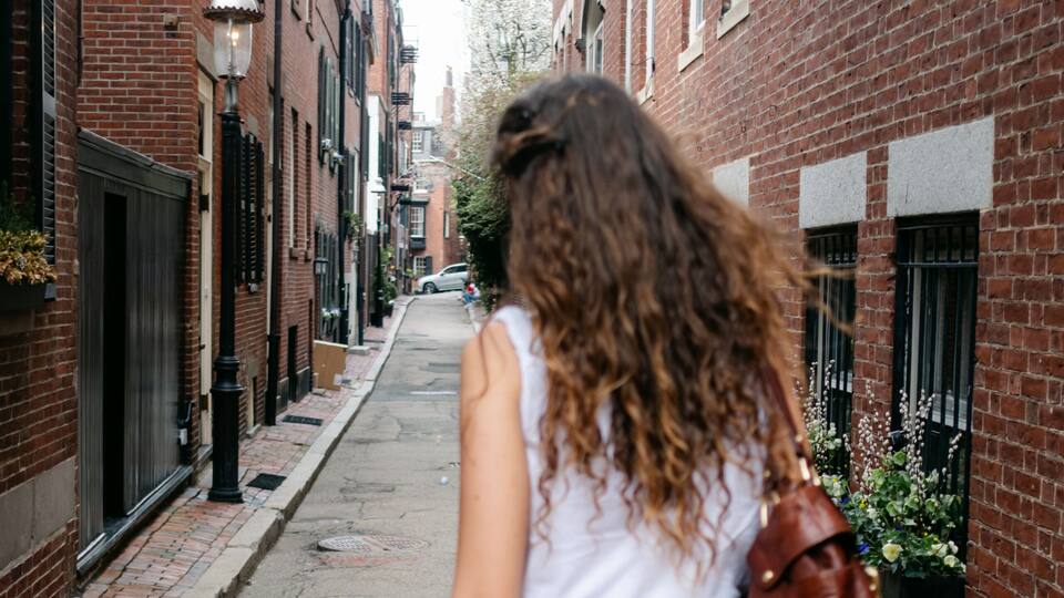 A woman walking down a brick-lined street with buildings on either side.