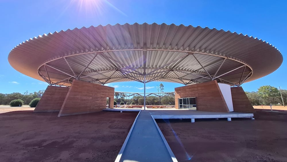 A modern pavilion with a large, curved roof supported by two brick pillars.