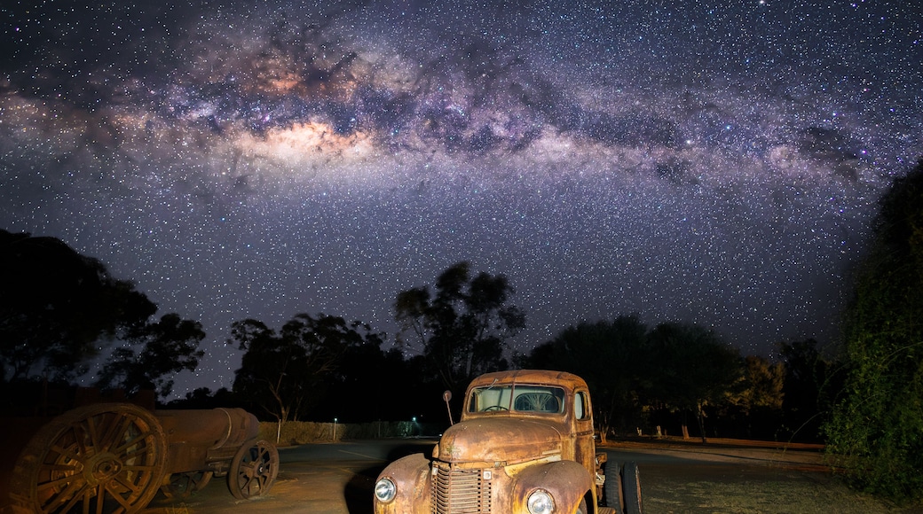 A vintage car parked under a starry night sky with the Milky Way visible.