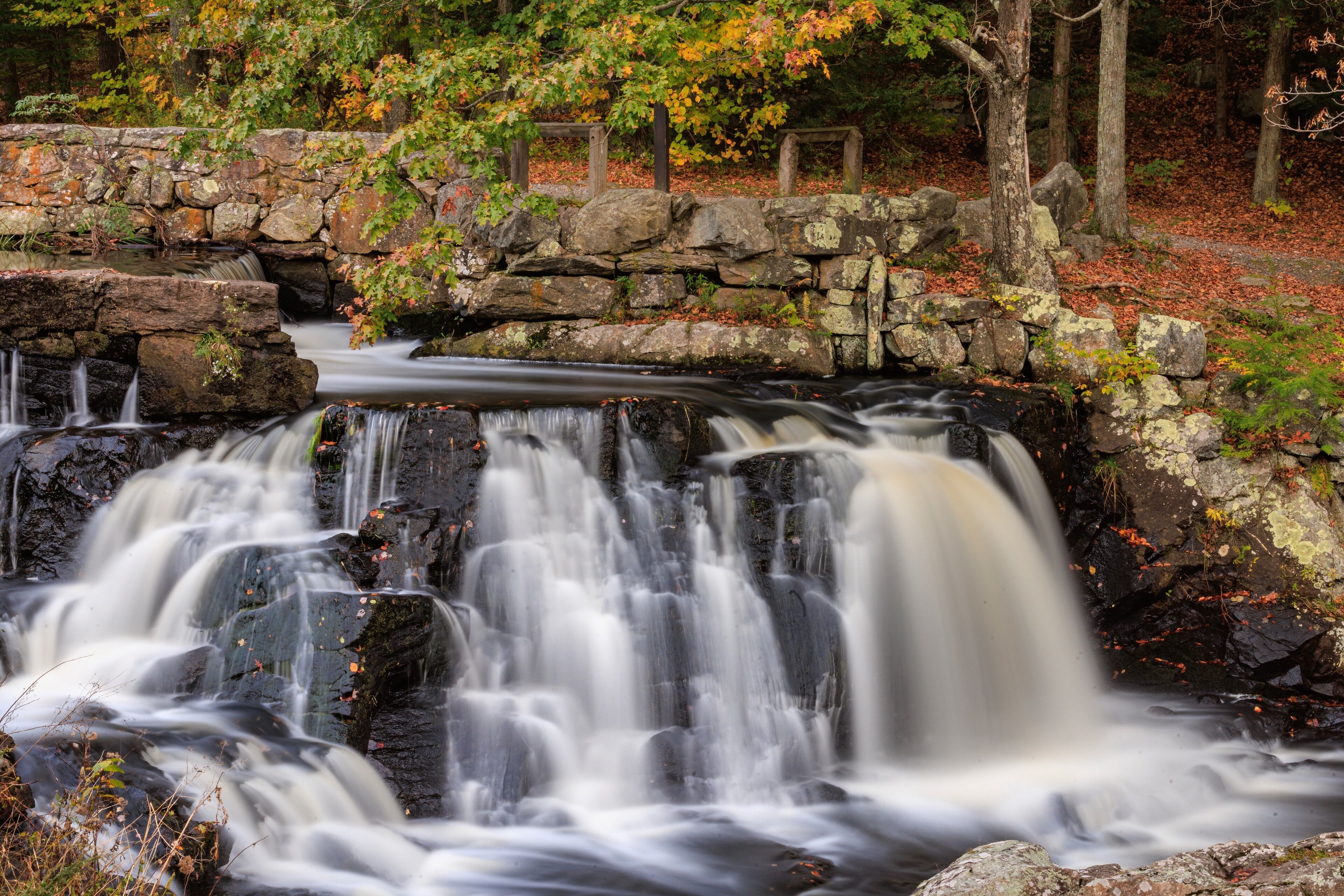 Small waterfall over a stone dam surrounded by autumn foliage