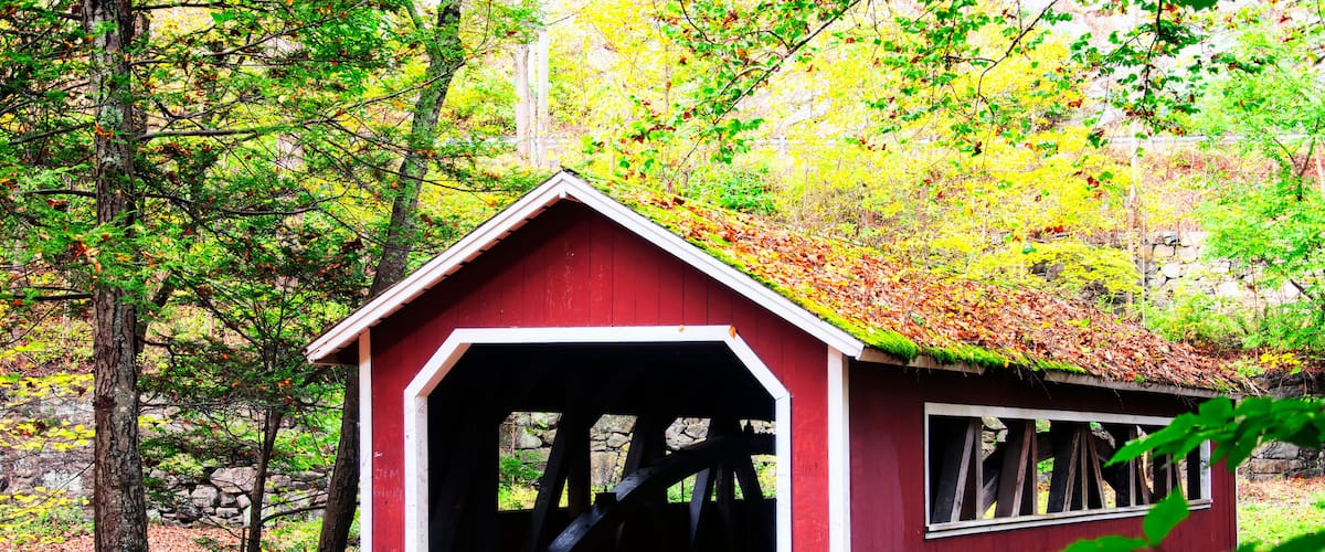 A red covered bridge with a wooden walkway, surrounded by autumn foliage and trees.