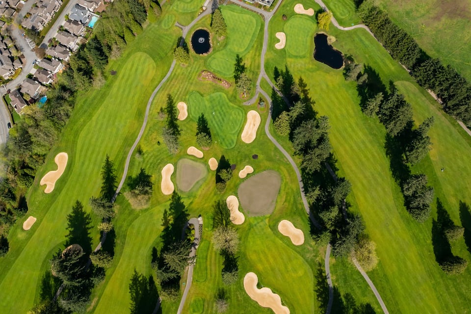 An aerial view of a golf course with sand bunkers, a pond, and surrounding residential buildings.