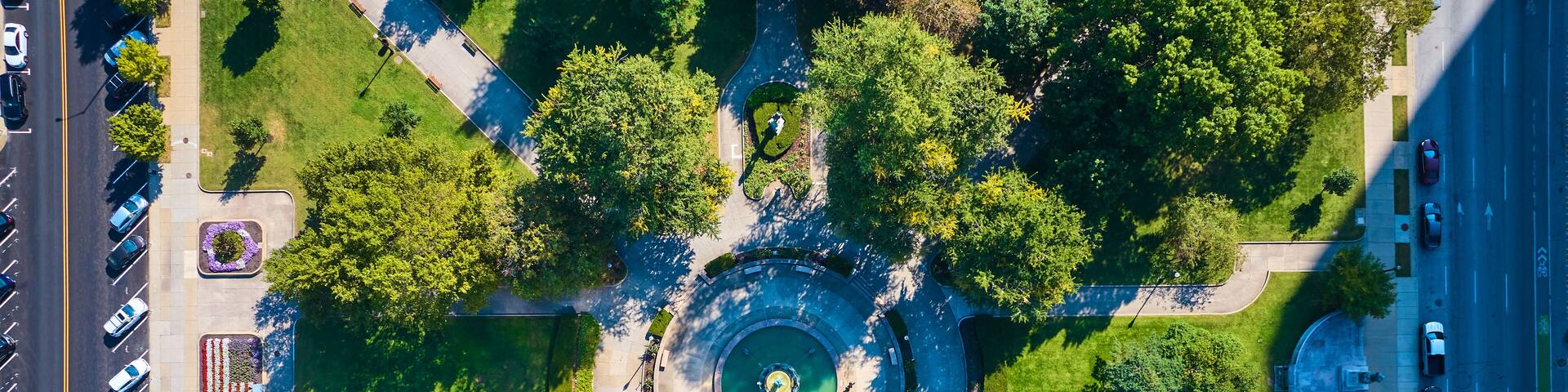 An aerial view of a roundabout with a central fountain surrounded by greenery and trees.