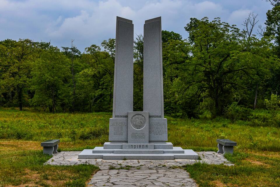 A monument with inscriptions and the word "INDIANA" at its base, surrounded by greenery.