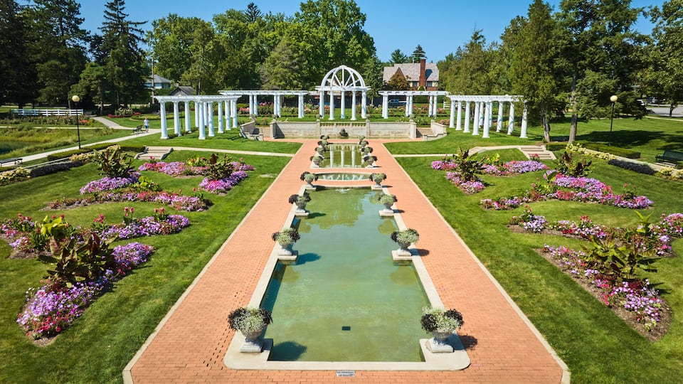 A formal garden with a central water feature, symmetrical flower beds, and white pergolas.