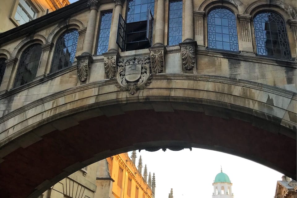 An arched bridge with ornate details and a building with a green dome in the background.