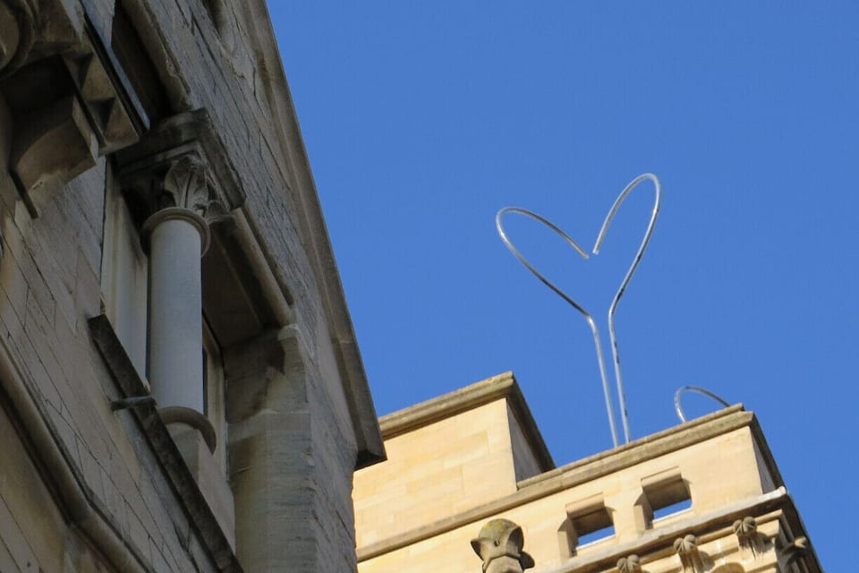 A building with classical architecture and a heart-shaped metal sculpture against a clear blue sky.