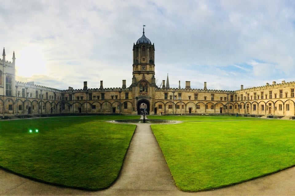 A historic courtyard with a central tower, surrounded by arched buildings and a well-maintained lawn.