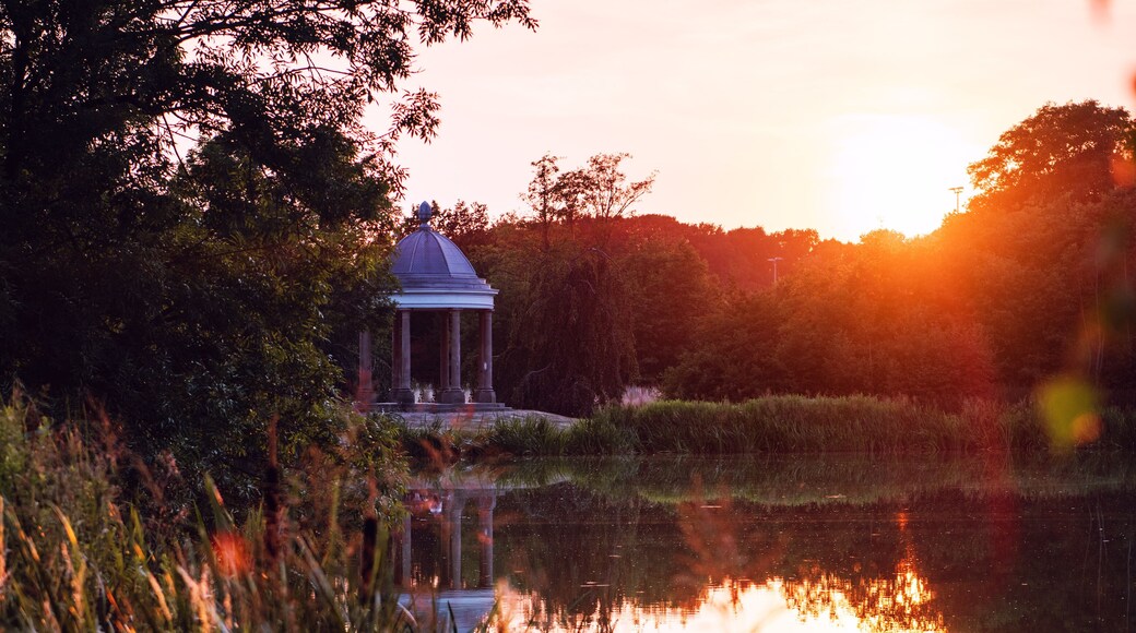 Historic pavilion building in a nature city park with a lake and water reflection at moody colorful orange sunset tones with lens flare. Braunschweig, Germany