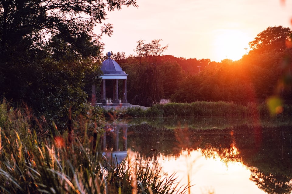 Un kiosque au bord d’un étang, au coucher du soleil.