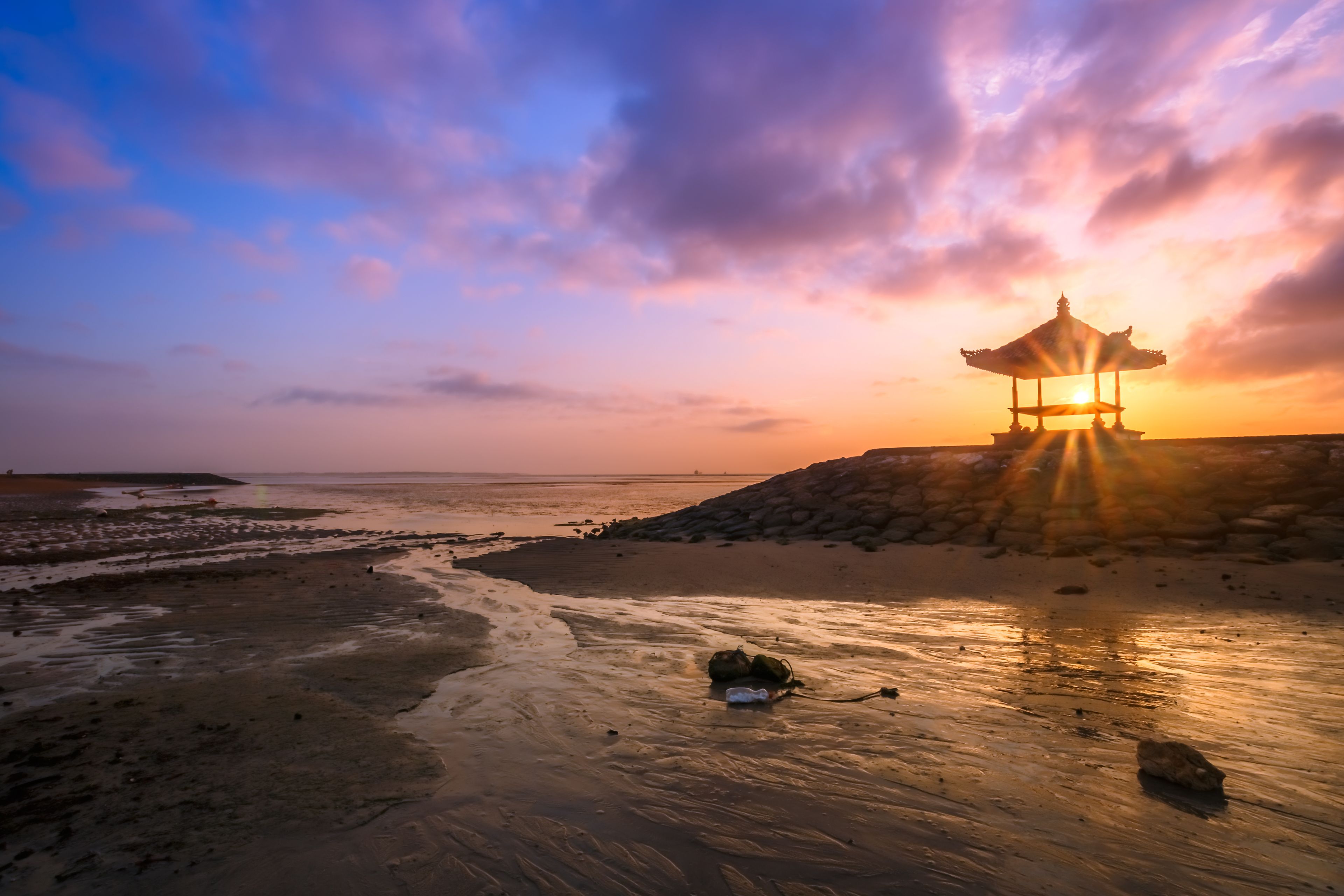 A sunset over a beach with a traditional pavilion.