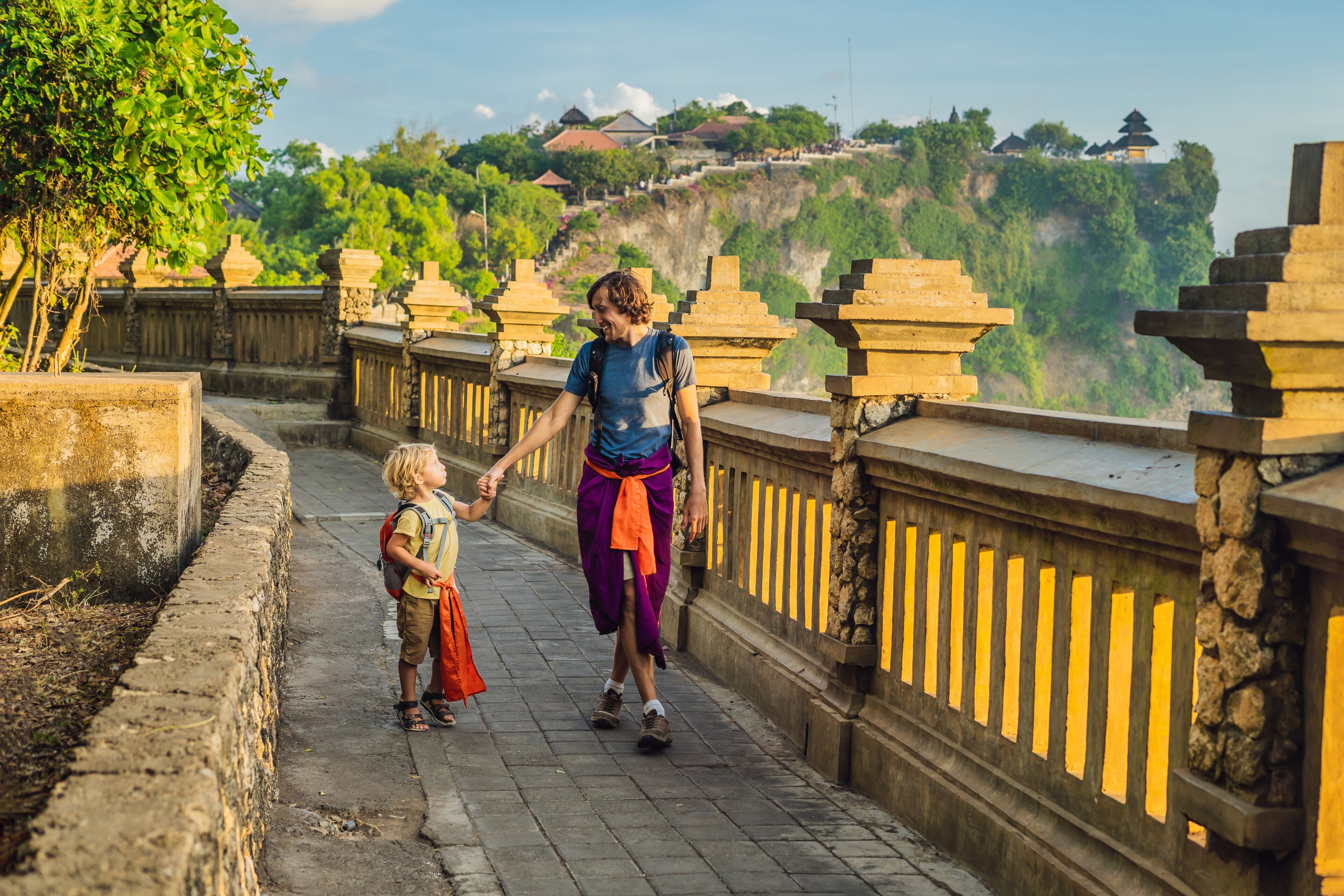 Dad and son travelers in Pura Luhur Uluwatu temple, Bali, Indonesia. Amazing landscape - cliff with blue sky and sea. Traveling with kids concept