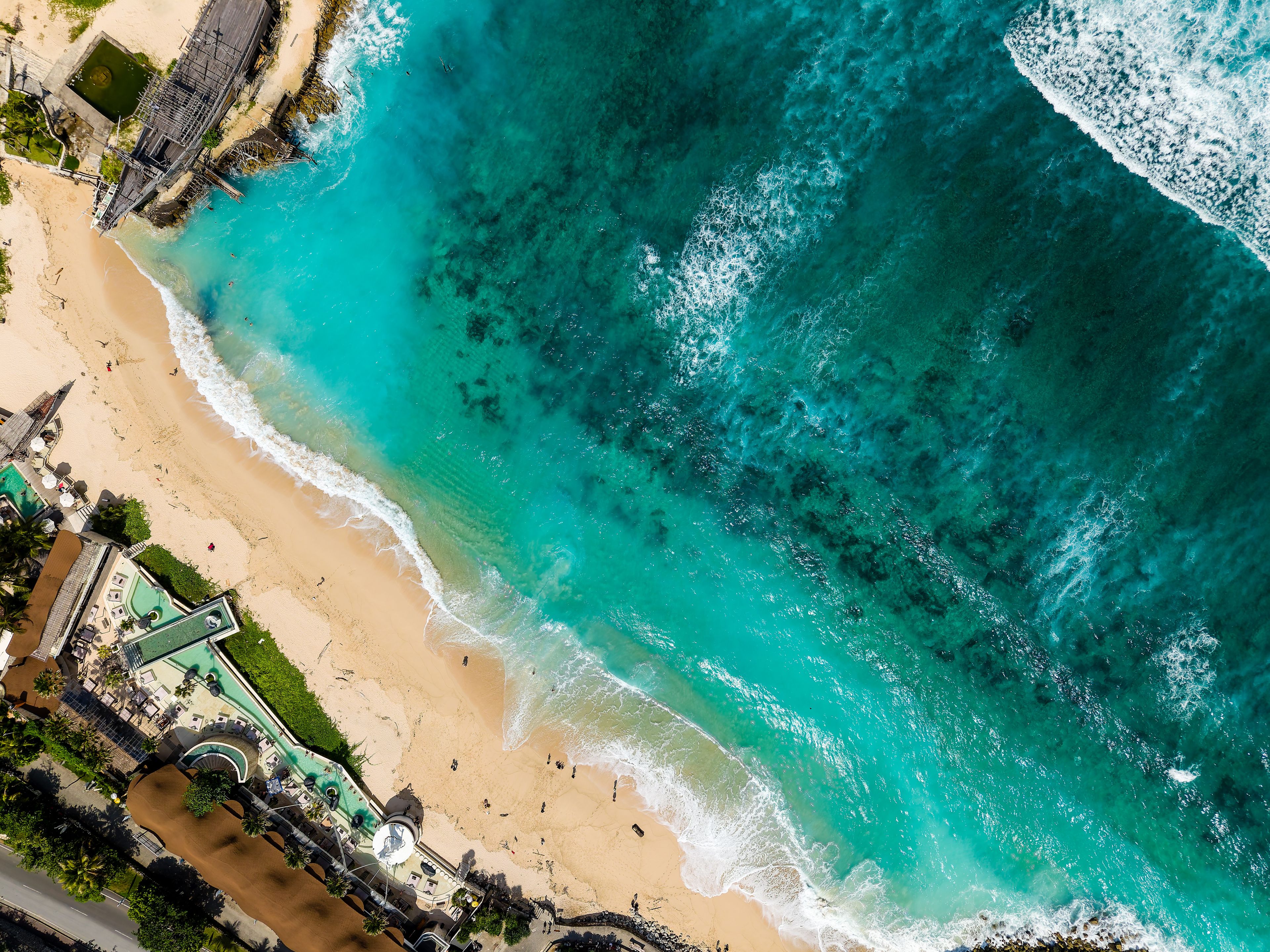 Top-down aerial shot of Nusa Dua coastline featuring blue water, waves, and beach clubs