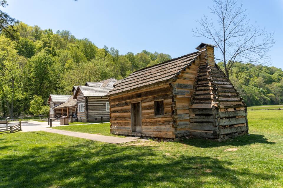 A rustic log cabin with a steep roof, surrounded by lush green grass and trees.