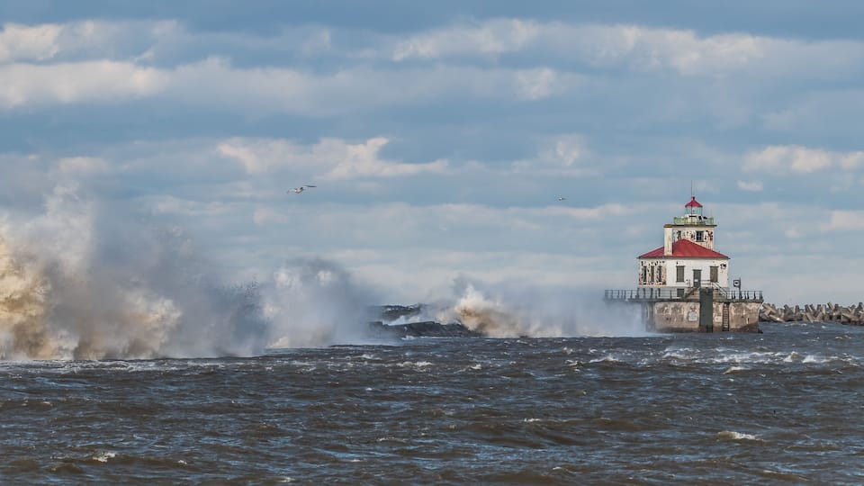 A lighthouse by a turbulent sea with waves crashing against it.