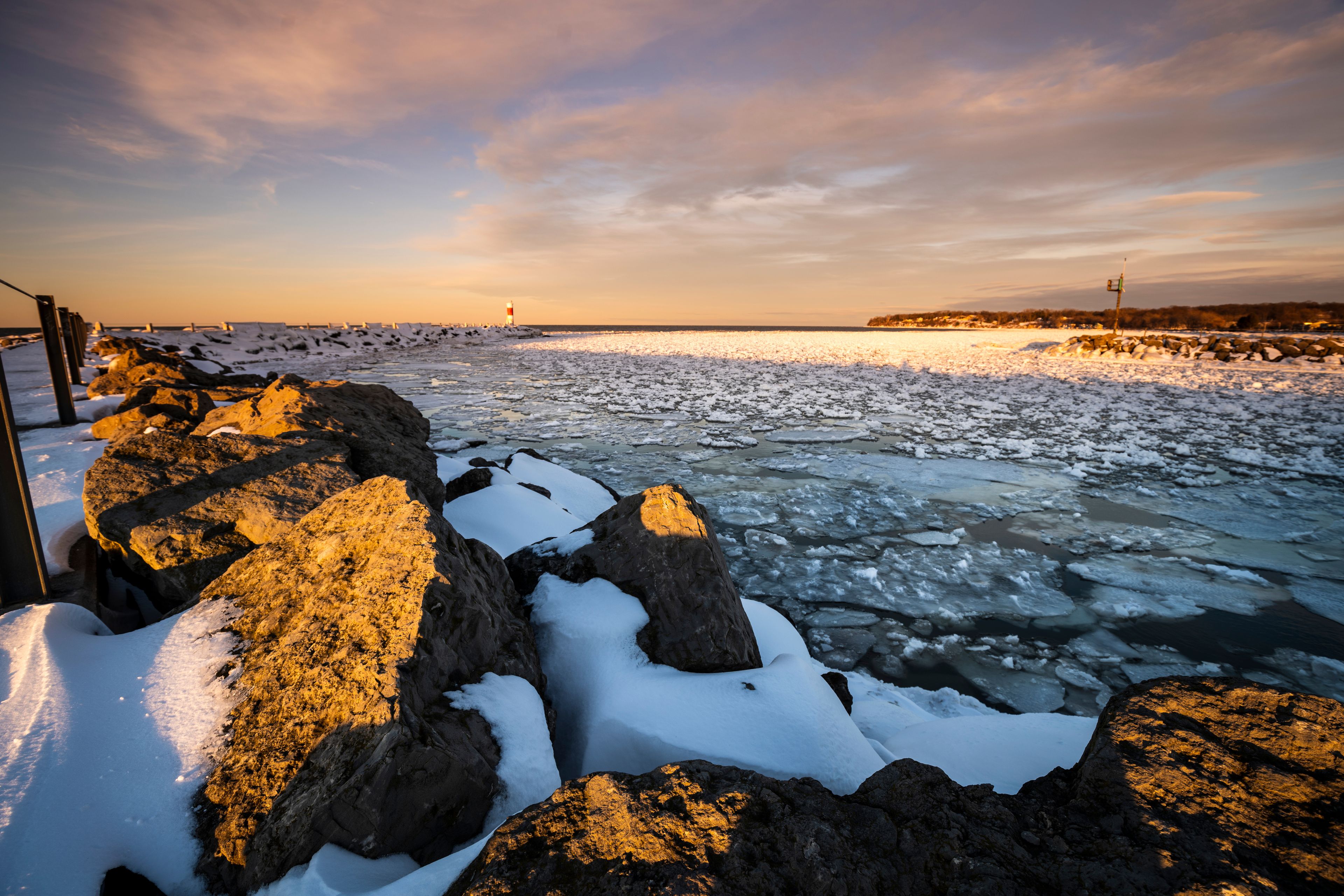 A frozen river with ice floes, a rocky shoreline, and a distant lighthouse.