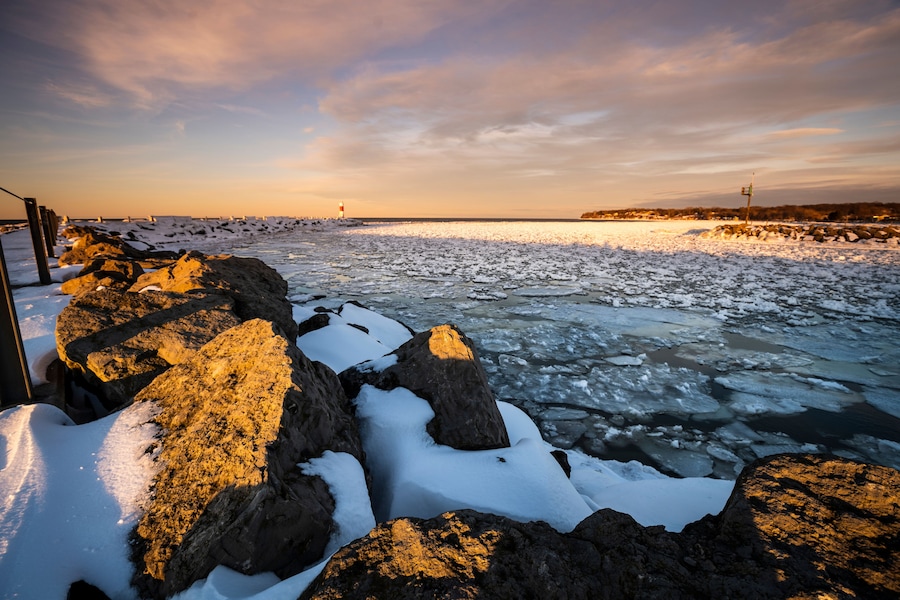 A frozen river with ice floes, a rocky shoreline, and a distant lighthouse.