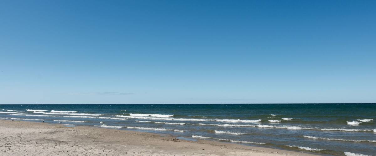 A beach with waves, clear sky, and distant horizon.