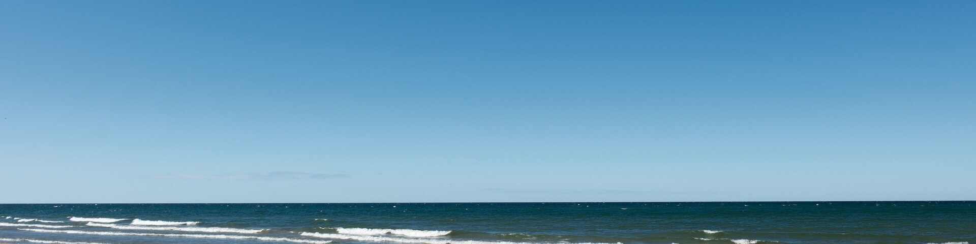 A beach with waves, clear sky, and distant horizon.