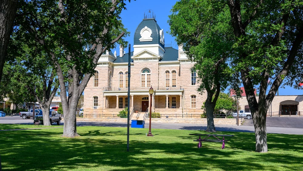 A historic building with a green dome and arched windows, surrounded by lush green trees and a well-maintained lawn.