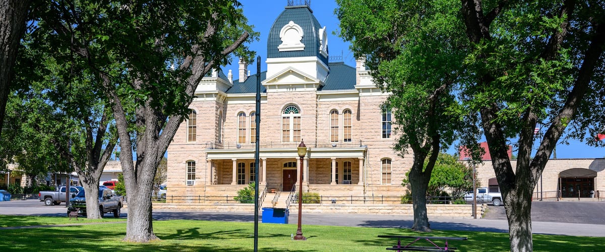 A historic building with a green dome and arched windows, surrounded by lush green trees and a well-maintained lawn.
