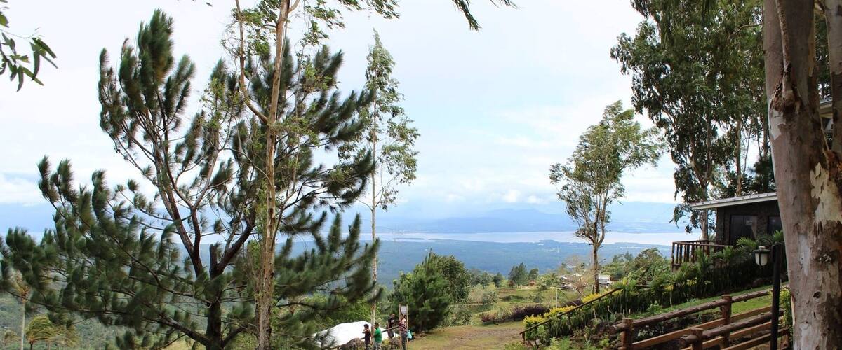 A mountainous landscape with a wooden fence, trees, and a distant view of a body of water.