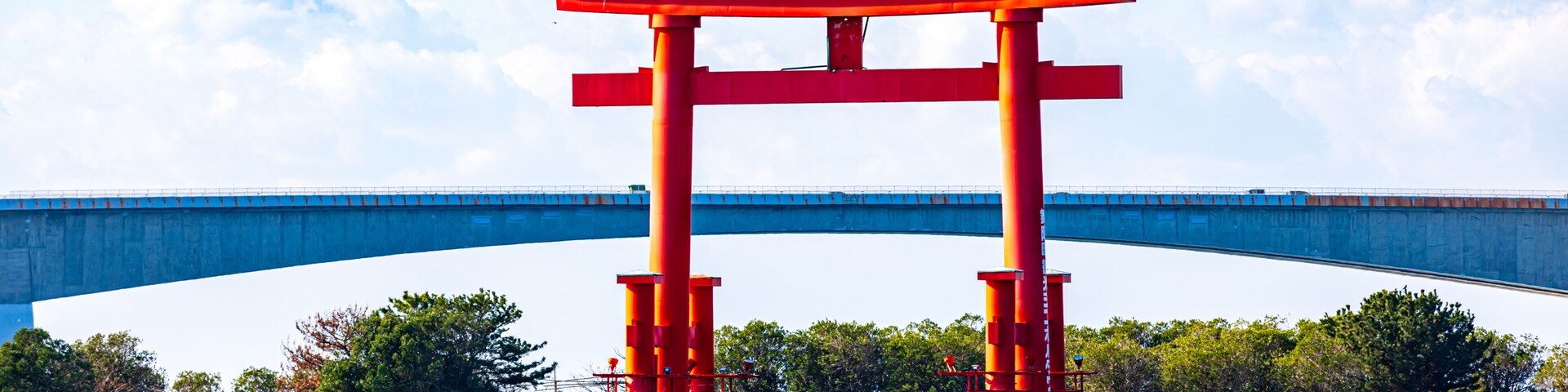Un torii rojo en el agua, con un puente al fondo.