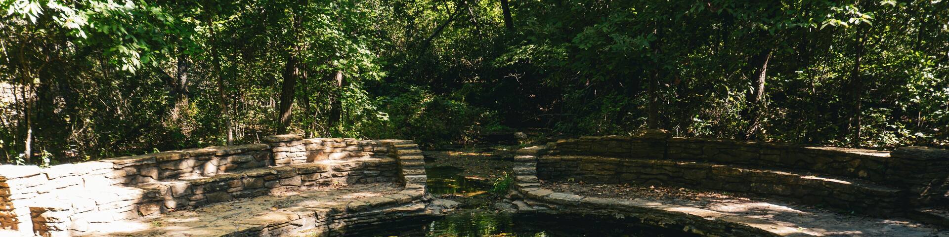 A stone circular pond surrounded by a stone wall, with trees in the background.