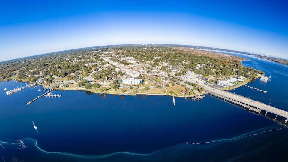 An aerial view of a coastal town with a marina, a bridge, and a lighthouse.