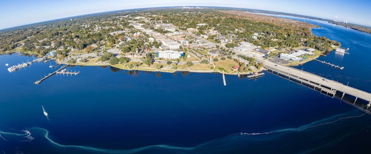 An aerial view of a coastal town with a marina, a bridge, and a lighthouse.