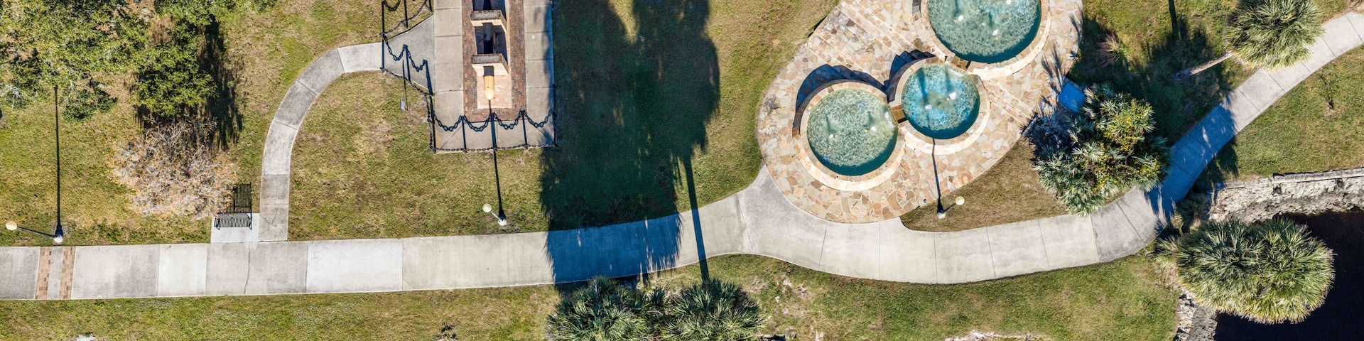 An aerial view of a park with a fountain, a small building, and a curved pathway.