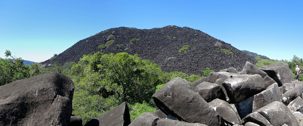A volcanic mountain with a forested base and large boulders in the foreground.