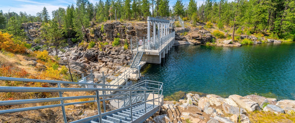 The closed dam at Falls Park showing the rocky riverbank and cliffs along the Spokane River at summer in the rural town of Post Falls, Idaho.
