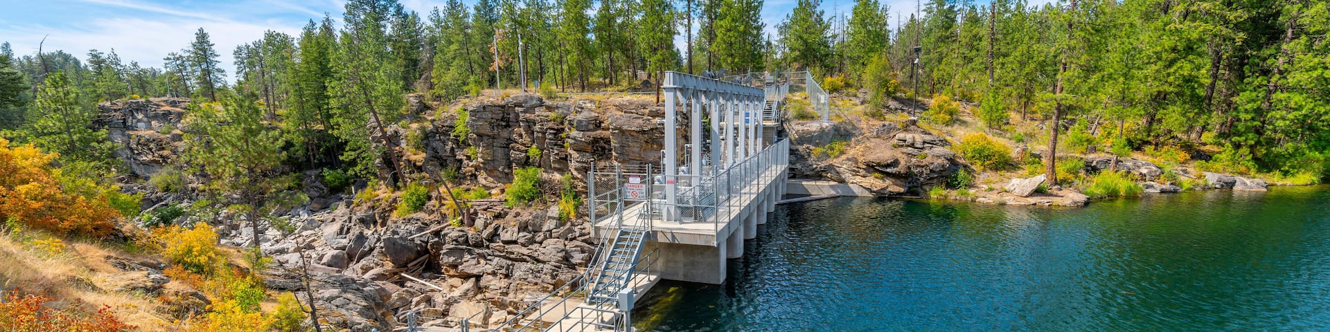 The closed dam at Falls Park showing the rocky riverbank and cliffs along the Spokane River at summer in the rural town of Post Falls, Idaho.
