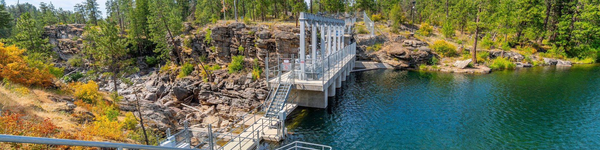 The closed dam at Falls Park showing the rocky riverbank and cliffs along the Spokane River at summer in the rural town of Post Falls, Idaho.