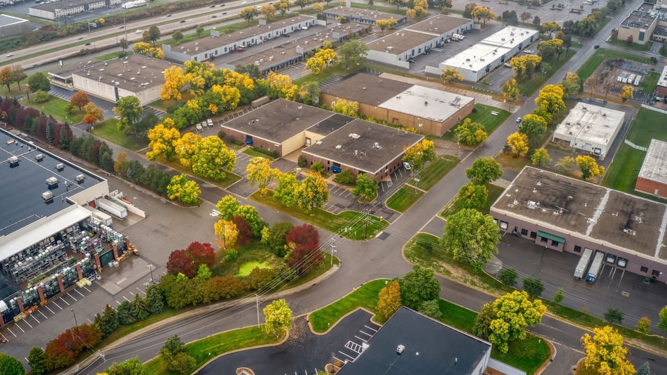 An aerial view of a commercial area with multiple buildings, parking lots, and trees with autumn foliage.