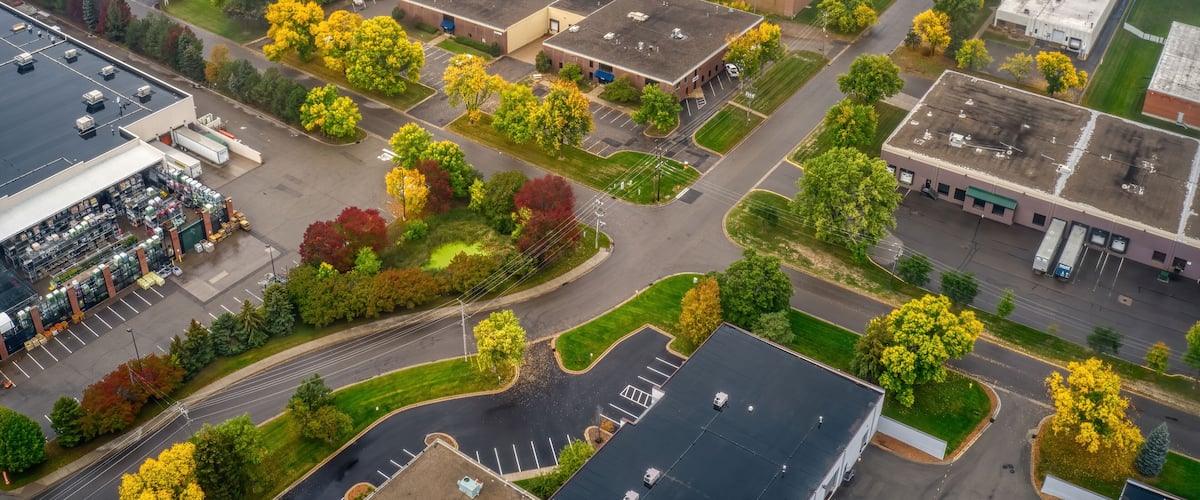 An aerial view of a commercial area with multiple buildings, parking lots, and trees with autumn foliage.