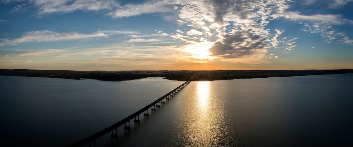 A sunset over a calm river with a bridge extending into the distance.