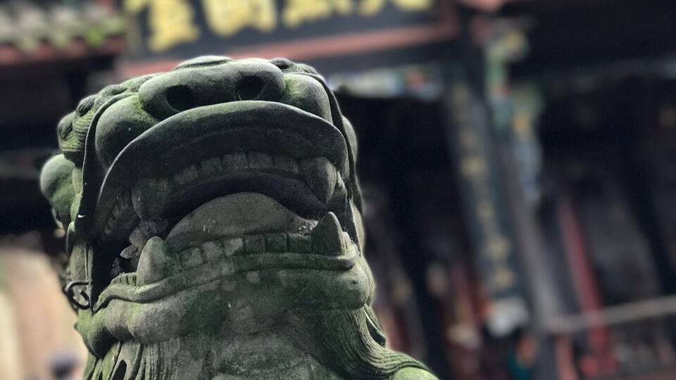 Eine Steinstatue eines Löwen vor einem traditionellen chinesischen Gebäude mit chinesischen Schriftzeichen.