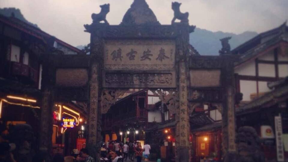 A traditional gate with lion statues, a crowd of people, and a mountainous backdrop.