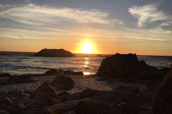 Ein Sonnenuntergang über einer felsigen Küstenlinie, wobei sich die Sonne im Wasser spiegelt.