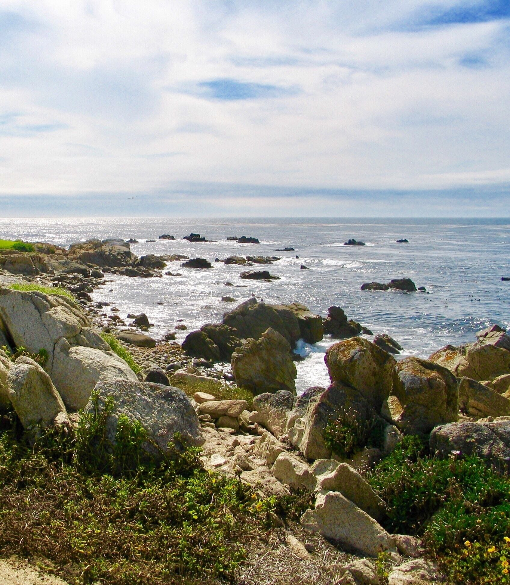 A rocky coastline with waves crashing against large boulders and a clear sky.
