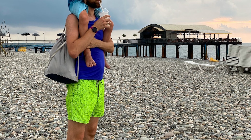 Father Carrying Son On Shoulders Drinking Milkshakes On Pebble Beach Under Dramatic Storm Sky During Summer Walk