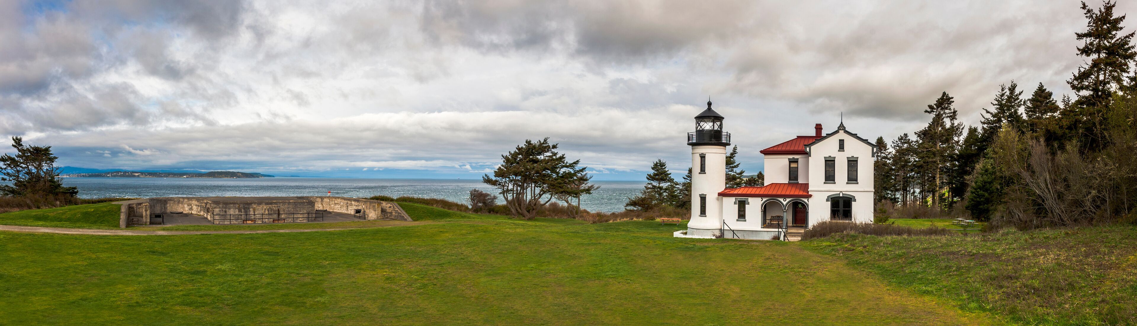 A coastal lighthouse with a red roof, a stone fortification, and a grassy foreground.