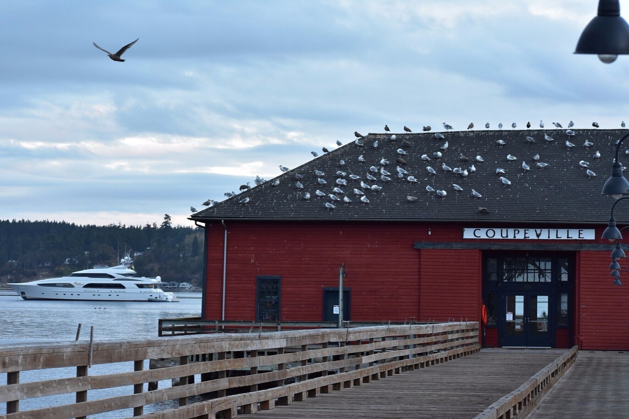 A red building named COUPEVILLE with a dock and a white yacht in the background.
