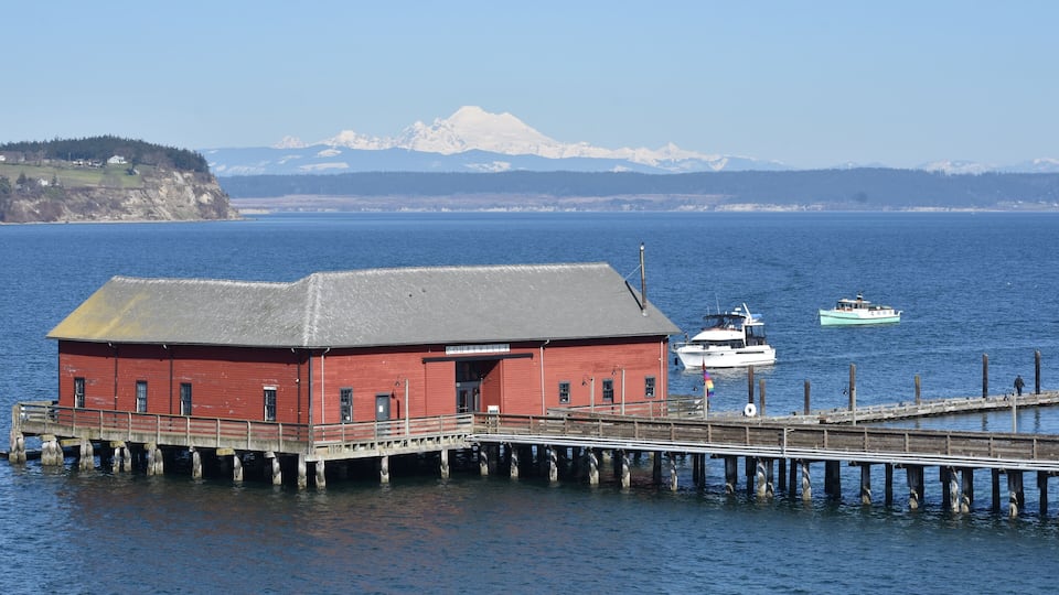 A red building on stilts by a calm body of water with a boat docked nearby.