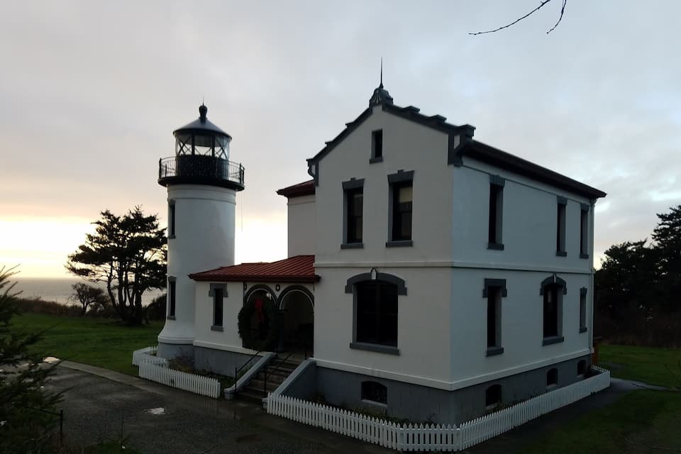 A white lighthouse with a red roof next to a white building with a red roof.