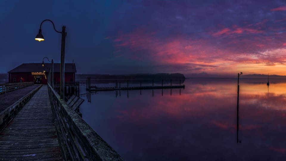 A wooden pier extending into calm waters at sunset with a colorful sky.